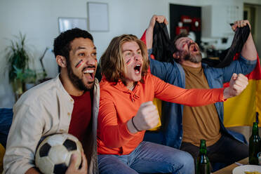 Happy German football fans friends watching football at home and celebrating success - HPIF02089