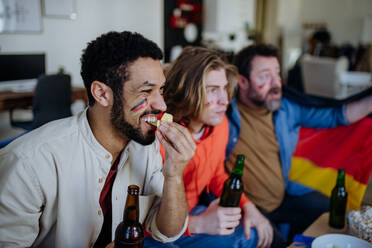 Nervous football fans friends watching a German national team in live soccer match on TV at home - HPIF02096