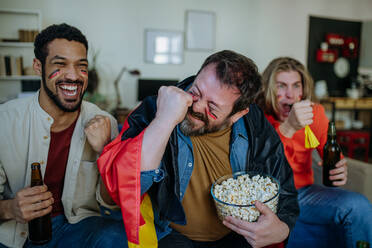 Glückliche deutsche Fußballfans, die zu Hause Fußball schauen und Popcorn essen. - HPIF02105