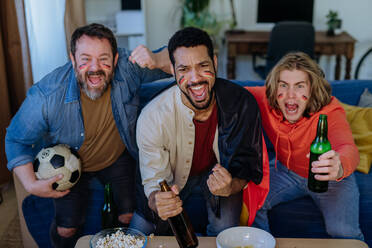 Glückliche deutsche Fußballfans, die zu Hause Fußball schauen und Popcorn essen. - HPIF02109