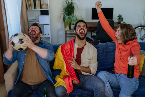 Glückliche deutsche Fußballfans, die zu Hause Fußball schauen und Popcorn essen. - HPIF02113