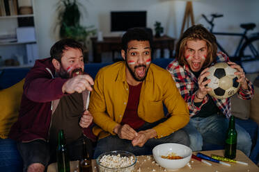 Nervous football fans friends watching live soccer match on a TV at home - HPIF02128