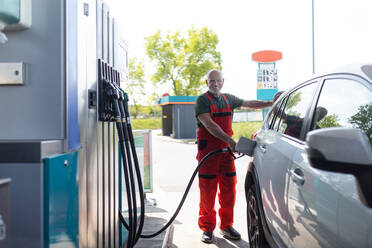 Ein älterer Arbeiter steht an einer Tankstelle und betankt ein Auto. - HPIF02154