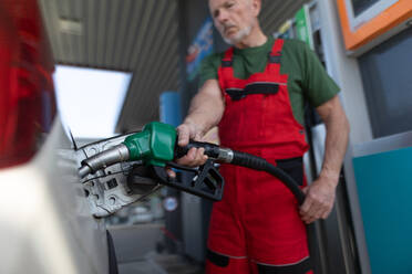 Ein älterer Arbeiter steht an einer Tankstelle und betankt ein Auto. - HPIF02157