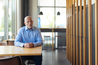 Ein trauriger älterer Mann sitzt an einem leeren Tisch mit unscharfen Cafe Interieur im Hintergrund - HPIF02171