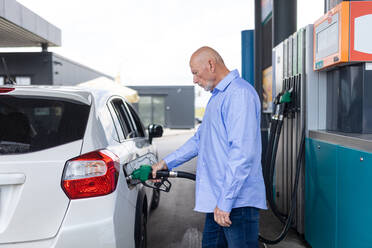 Ein älterer Geschäftsmann steht an einer Tankstelle und betankt sein Auto. - HPIF02182