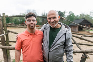 A happy senior father with his adult son with Down syndrome at ranch looking at camera. - HPIF02194