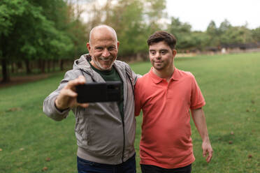 Ein glücklicher älterer Vater mit seinem kleinen Sohn mit Down-Syndrom macht ein Selfie im Park. - HPIF02199