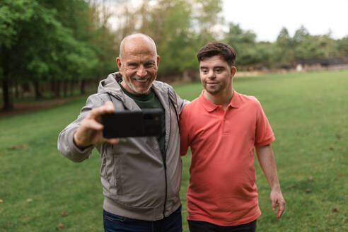 Ein glücklicher älterer Vater mit seinem kleinen Sohn mit Down-Syndrom macht ein Selfie im Park. - HPIF02199