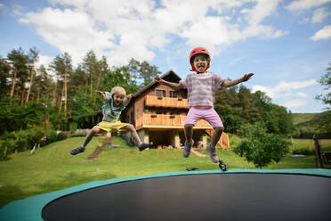 A little siblings enjoy jumping on trampoline - outside in backyard - HPIF02206