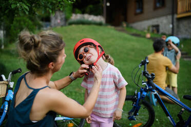 Eine junge Mutter mit ihrer kleinen Tochter bereitet sich auf eine Fahrradtour vor, indem sie die Helme aufsetzen. - HPIF02207