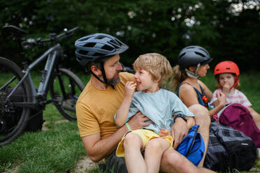 A young family with little children resting after bike ride, sitting on grass in park in summer. - HPIF02213