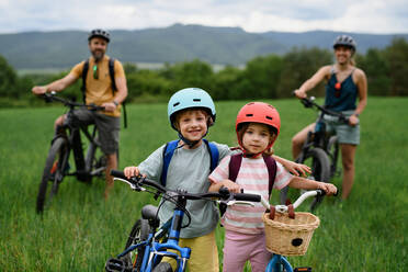 Porträt einer jungen Familie mit kleinen Kindern, die Rad fahren, stehen und sich mit den Fahrrädern in der Natur ausruhen. - HPIF02214