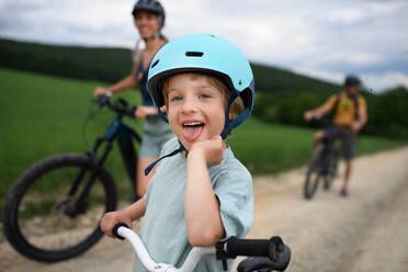 Ein Porträt der aufgeregten kleinen Jungen mit seiner Familie im Hintergrund Radfahren auf dem Weg im Park im Sommer - HPIF02216