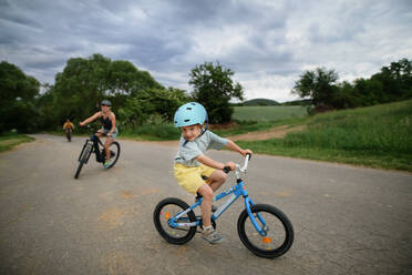 Ein Porträt der aufgeregten kleinen Jungen mit seiner Familie im Hintergrund Radfahren auf dem Weg im Park im Sommer - HPIF02218