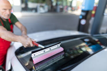 Ein älterer Angestellter wäscht eine Autoscheibe an einer Tankstelle. - HPIF02222