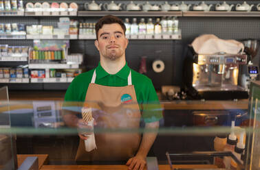 A happy waiter with Down syndrome serving baguette and passing it to costumer in cafe at gas station. - HPIF02226