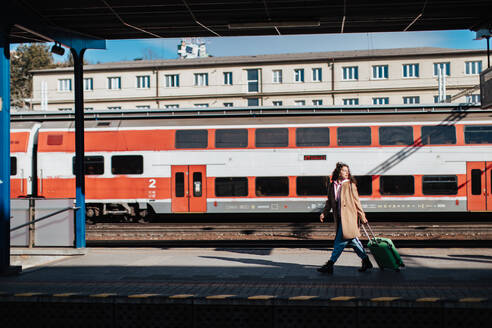 Eine junge Reisende mit Gepäck, die auf dem Bahnsteig auf den Zug wartet, mit dem Zug im Hintergrund. - HPIF02263