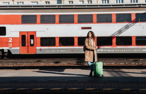 Eine junge Reisende mit Gepäck, die auf dem Bahnsteig auf den Zug wartet, mit dem Zug im Hintergrund. - HPIF02264