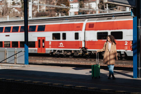 Eine junge Reisende mit Gepäck, die auf dem Bahnsteig auf den Zug wartet, mit dem Zug im Hintergrund. - HPIF02265