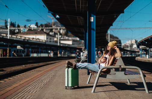 Eine junge Reisende, die mit ihrem Gepäck allein auf dem Bahnsteig sitzt. - HPIF02272