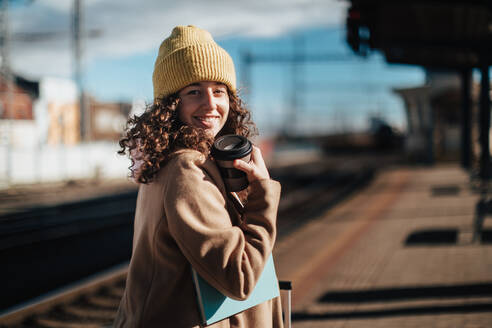 Ein Porträt von glücklichen jungen Reisenden Frau mit Kaffee und Gepäck am Bahnhof Plattform - HPIF02274