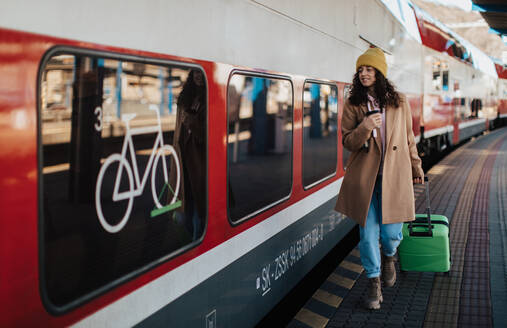 Eine glückliche junge Reisende Frau mit Gepäck und Tasse Kaffee Einsteigen in den Zug am Bahnhof Bahnsteig - HPIF02275