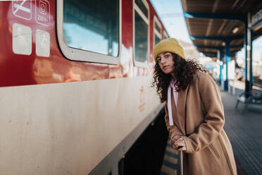 Eine junge Reisende Frau mit Gepäck steht am Bahnsteig und steigt in den Zug ein - HPIF02276