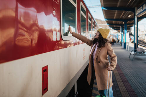 Eine junge Reisende mit Gepäck steht auf dem Bahnsteig und verabschiedet sich, indem sie jemandem im Zug zuwinkt - HPIF02277