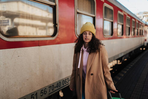 Eine junge Reisende Frau mit Gepäck steht am Bahnsteig und steigt in den Zug ein - HPIF02278