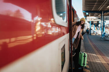Eine glückliche junge Reisende Frau mit Gepäck beim Aussteigen aus dem Zug am Bahnhof Plattform - HPIF02280