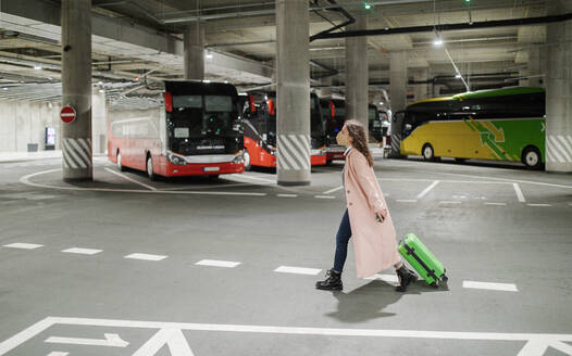 Alleinreisende Frau mit ffp2-Beatmungsgerät auf dem Weg zum Busbahnhof mit Gepäck, auf Reisen während der Covid-Pandemie. - HPIF02284