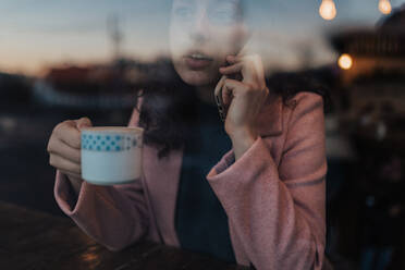 Eine junge Frau trinkt Tee und schaut aus dem Fenster eines Cafés, während sie ihre Freizeit alleine genießt - HPIF02290