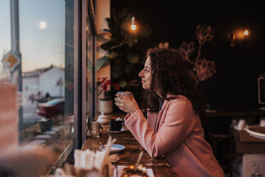 A young woman drinking tea and looking out of the cafe window while enjoying her leisure time alone - HPIF02291