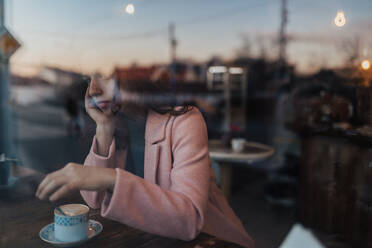 Traurige, nachdenkliche junge Frau, die einen Kaffee trinkt und aus dem Fenster des Cafés schaut. - HPIF02292