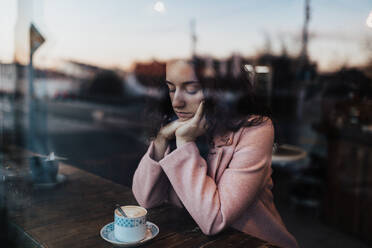 Traurige, nachdenkliche junge Frau, die einen Kaffee trinkt und aus dem Fenster des Cafés schaut. - HPIF02293