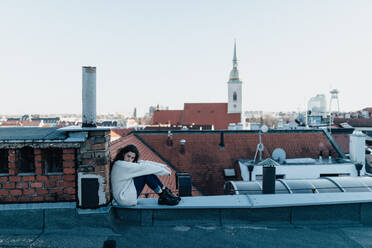 Eine unglückliche junge Frau, die sich ausruht und auf dem Dach mit Blick auf die Stadt sitzt. - HPIF02297