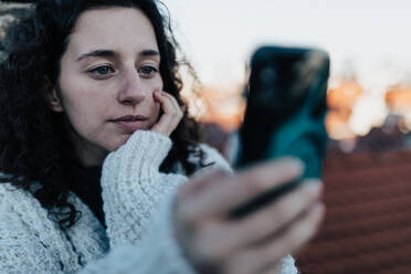 Eine unglückliche junge Frau ruht sich aus und sitzt auf dem Dach mit Blick auf die Stadt und macht ein Selfie. - HPIF02298