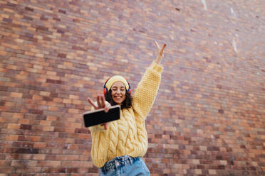 A portrait of happy young woman in front of brick wall in city street, looking at camera. - HPIF02305
