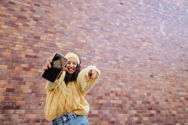 A portrait of happy young woman in front of brick wall in city street, looking at camera. - HPIF02306