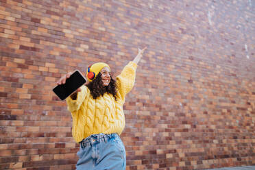 Ein Porträt einer glücklichen jungen Frau, die vor einer Backsteinmauer in der Stadt steht und in die Kamera schaut. - HPIF02307