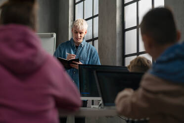 Ein Lehrer, der vor den Schülern steht und Notizen in einem Computerklassenzimmer in der Schule schreibt - HPIF02314