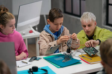 Eine Gruppe glücklicher Kinder mit ihrem Naturwissenschaftslehrer mit elektrischen Spielzeugen und Robotern im Robotik-Klassenzimmer - HPIF02331