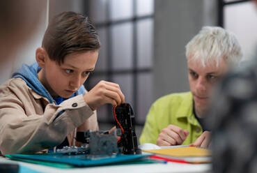 A group of happy kids with their science teacher with electric toys and robots at robotics classroom - HPIF02332