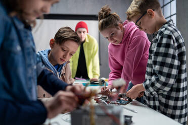Eine Gruppe glücklicher Kinder mit ihrem Naturwissenschaftslehrer mit elektrischen Spielzeugen und Robotern im Robotik-Klassenzimmer - HPIF02336