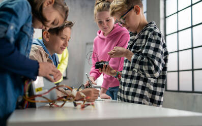 Eine Gruppe glücklicher Kinder mit ihrem Wissenschaftslehrer und elektrischen Spielzeugen, Robotern im Robotik-Klassenzimmer - HPIF02339