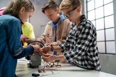 A group of happy kids with their science teacher with electric toys and robots at robotics classroom - HPIF02345