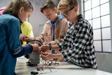 Eine Gruppe glücklicher Kinder mit ihrem Naturwissenschaftslehrer mit elektrischen Spielzeugen und Robotern im Robotik-Klassenzimmer - HPIF02345