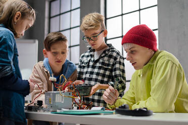 Eine Gruppe glücklicher Kinder mit ihrem Naturwissenschaftslehrer mit elektrischen Spielzeugen und Robotern im Robotik-Klassenzimmer - HPIF02348