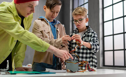 Eine Gruppe glücklicher Kinder mit ihrem Naturwissenschaftslehrer mit elektrischen Spielzeugen und Robotern im Robotik-Klassenzimmer - HPIF02351